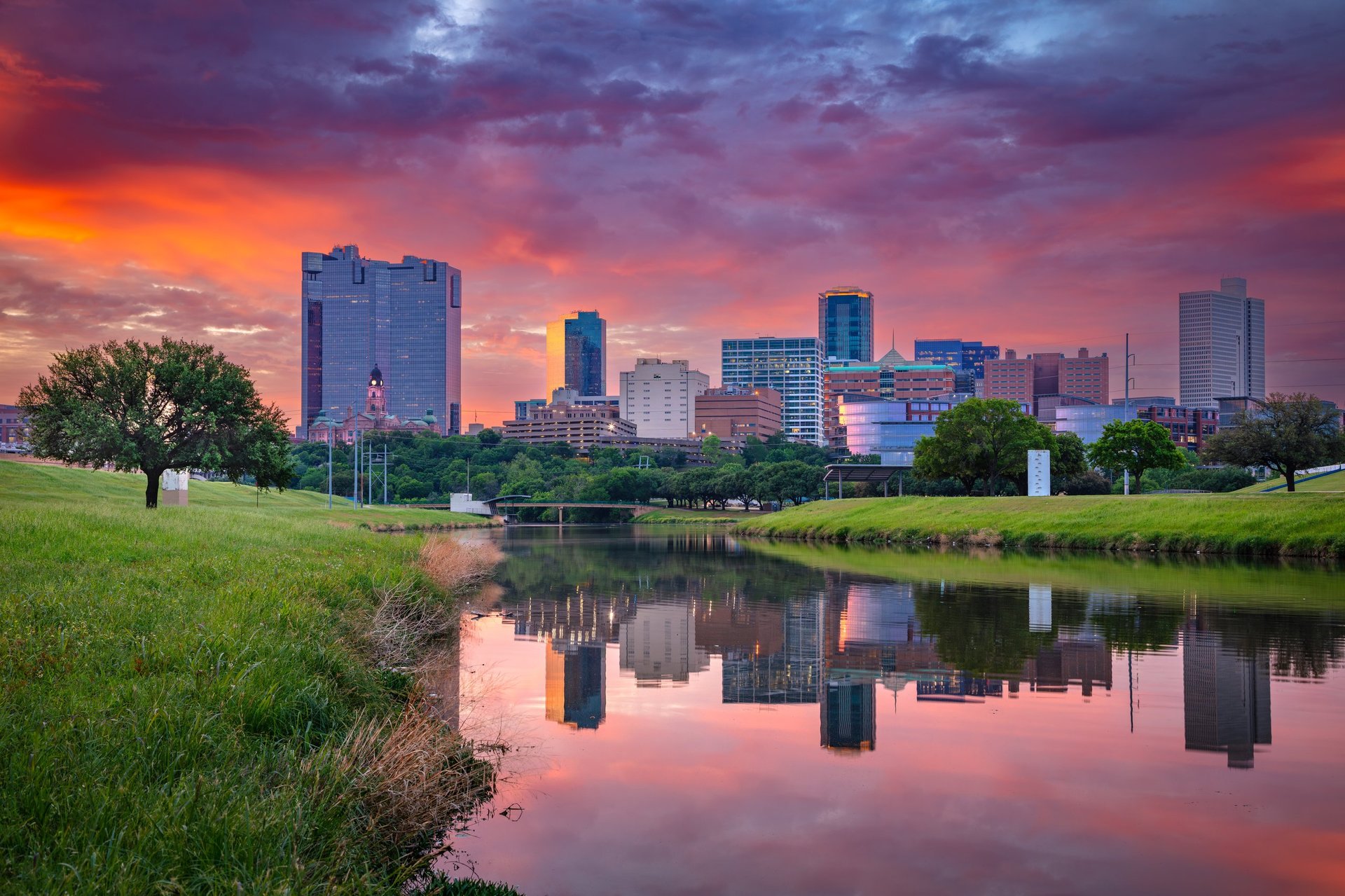 Downtown Fort Worth Texas skyline at sunrise with skyscrapers reflecting fiery sky and Trinity River